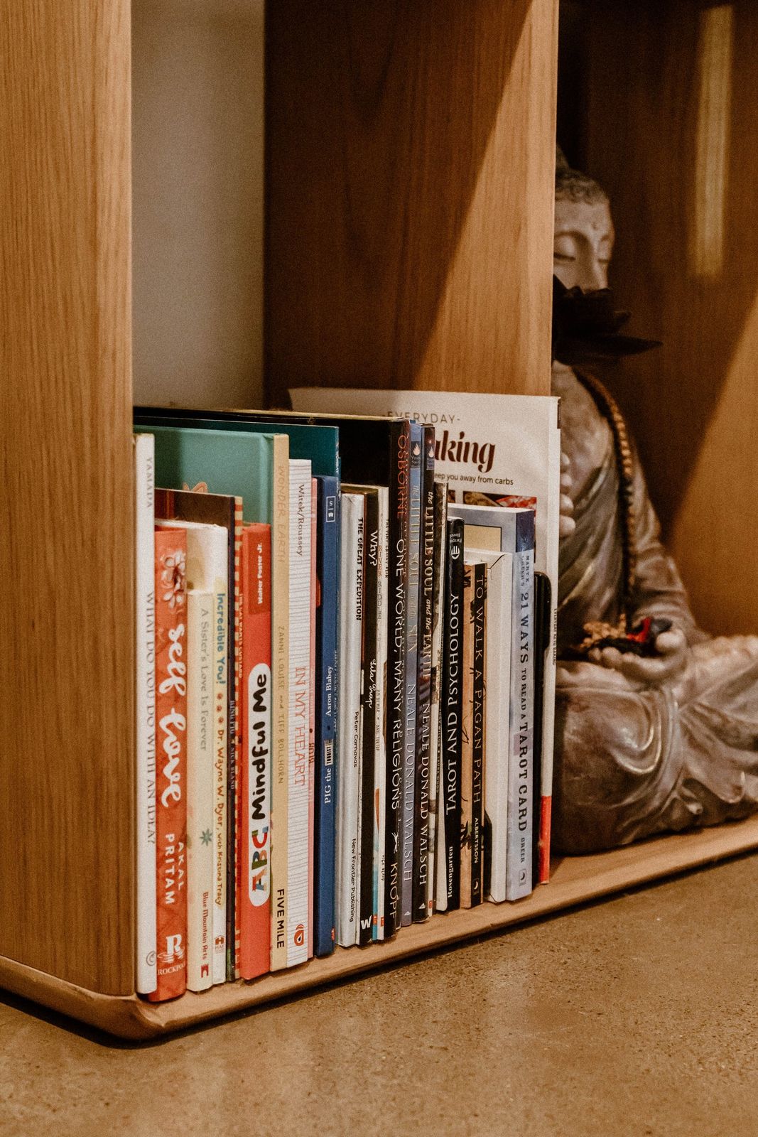 A low shelf of books beside a seated Buddha figure