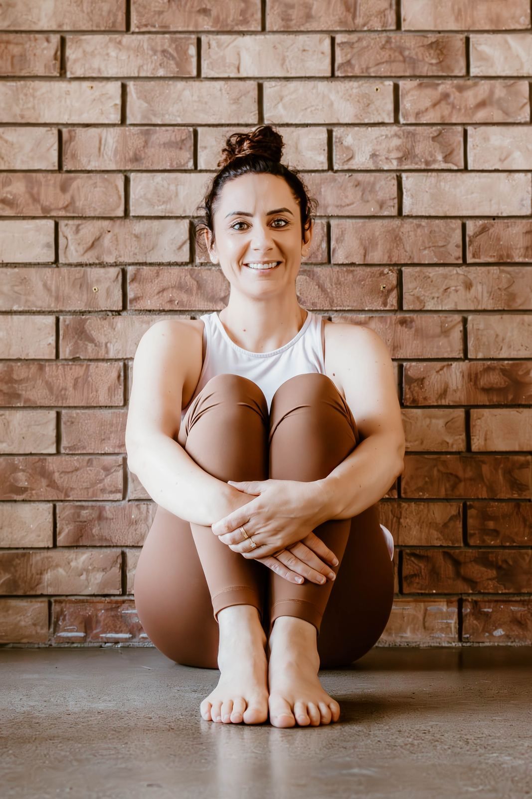 Emma seated in a yoga posture against a brick wall