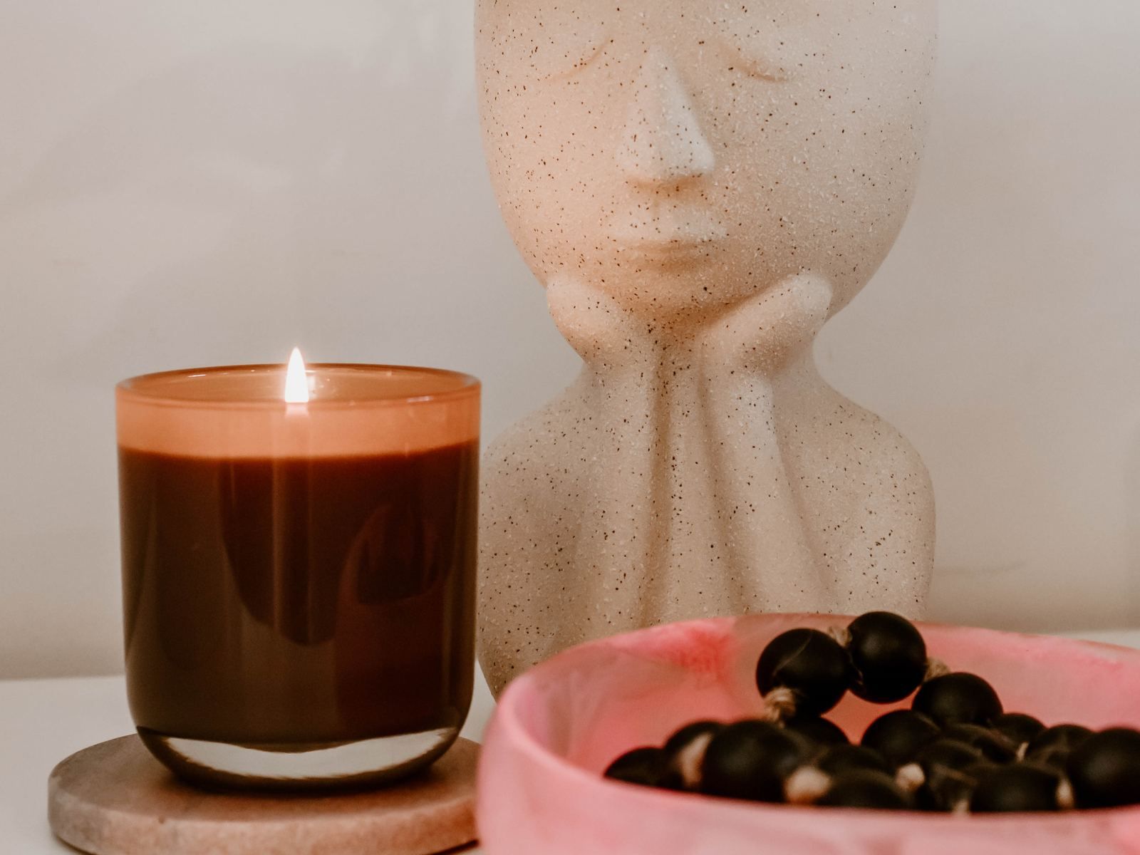 A lit candle beside a ceramic face and a bowl